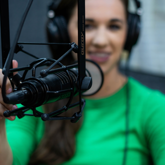 Woman in green shirt speaking into a studio microphone with headphones on