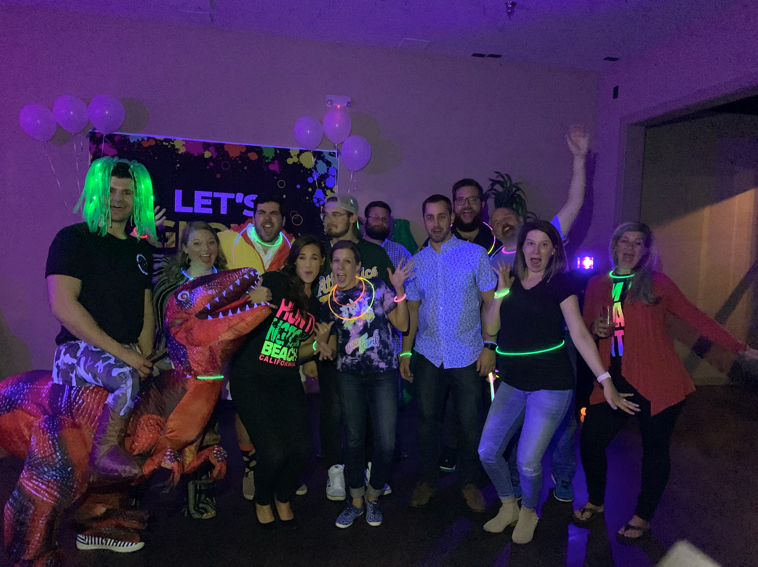 Group of people in colorful costumes posing at a Halloween party with purple lighting.