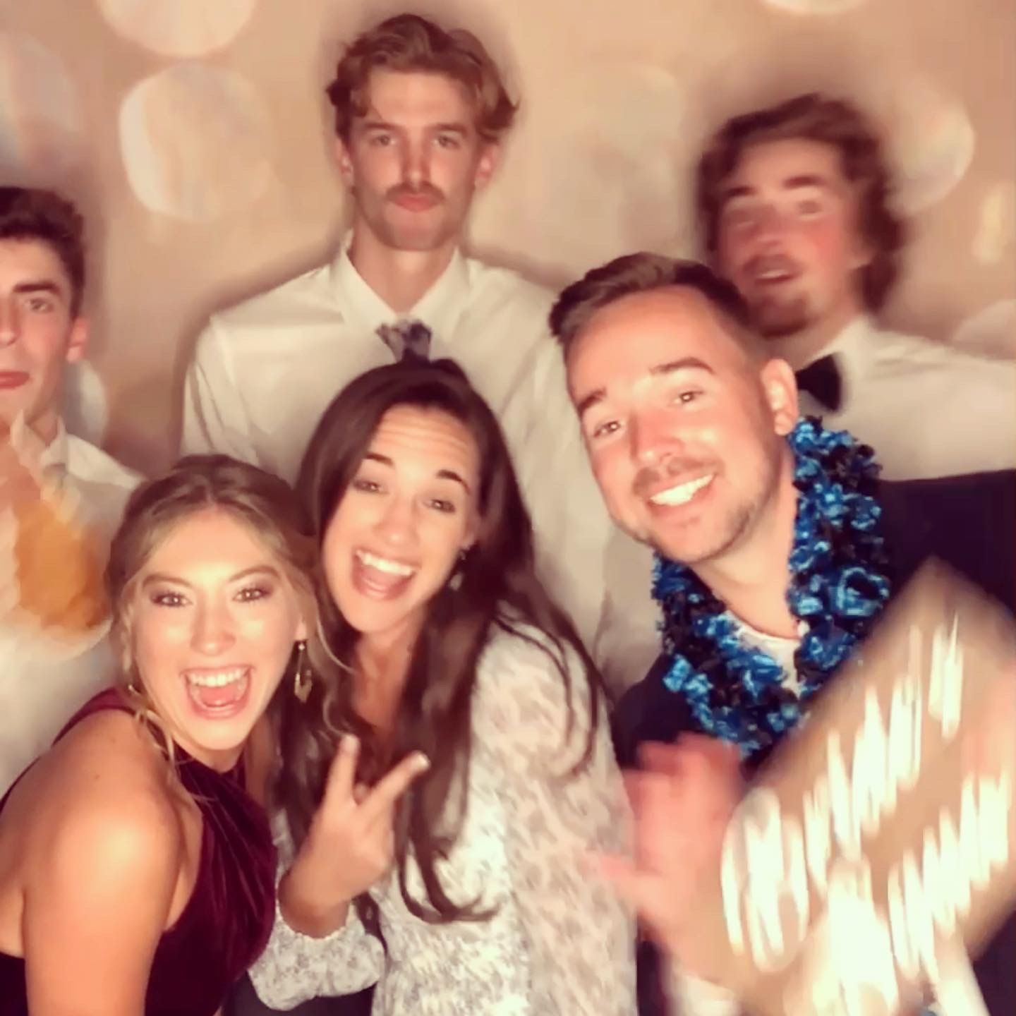 Five people smiling and posing at a party, with blue leis and a champagne bottle in the foreground.